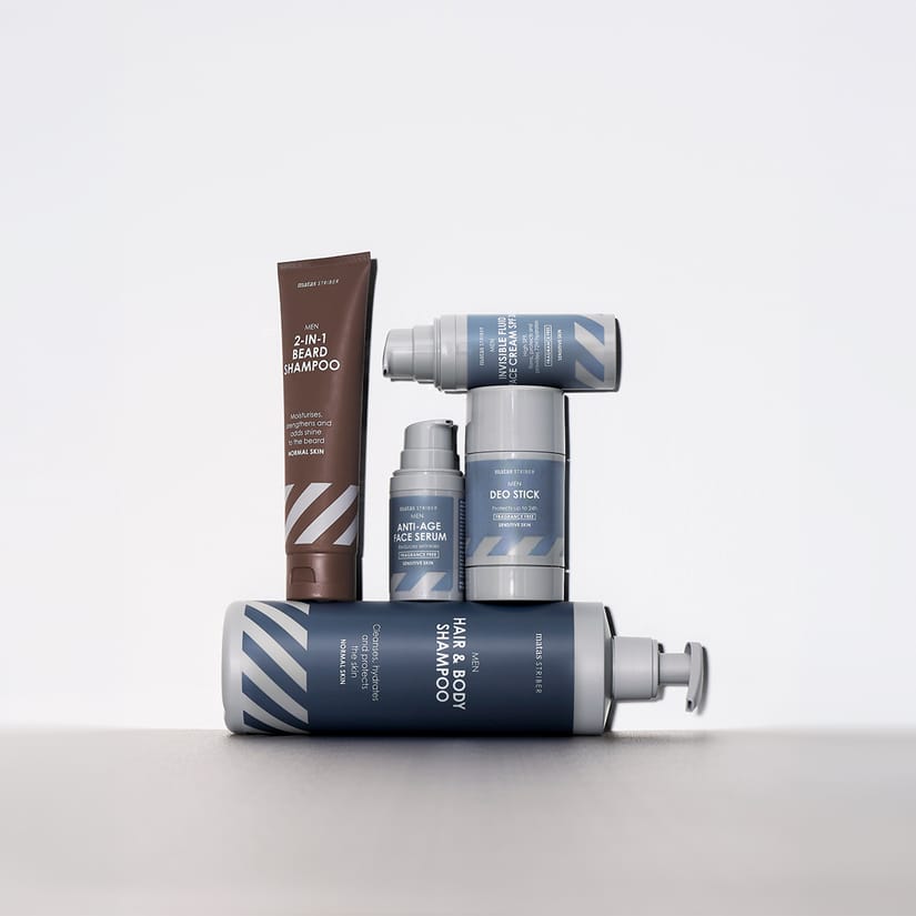 Her ses et udvalg af Matas Striber Men-produkter til hår-, skæg-, ansigts- og kropspleje. Produkterne omfatter 2-in-1 Beard Shampoo, Anti-Age Face Serum, Invisible Fluid Face Cream SPF 30, Deo Stick og Hair & Body Shampoo, arrangeret mod en lys baggrund.