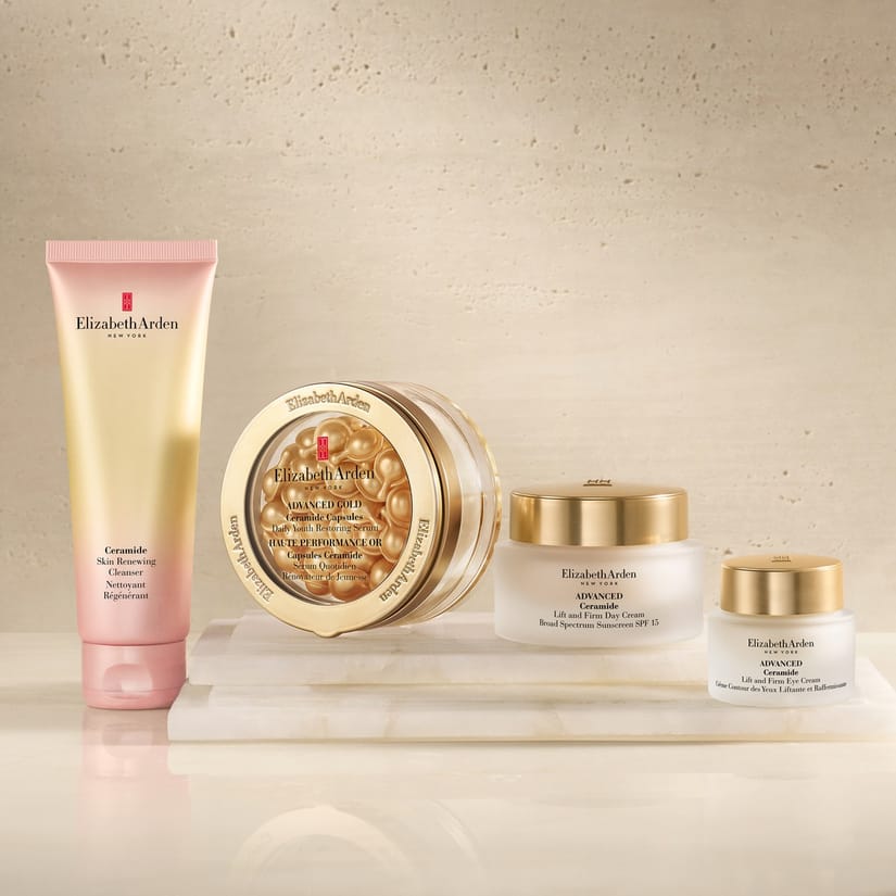 Her ses fire hudplejeprodukter fra Elizabeth Arden: Ceramide Skin Renewing Cleanser, Advanced Ceramide Capsules Daily Youth Restoring Serum, Advanced Ceramide Lift and Firm Day Cream SPF 15 og Advanced Ceramide Lift and Firm Eye Cream. Produkterne er arrangeret på en lys marmoreret overflade mod en beige baggrund.