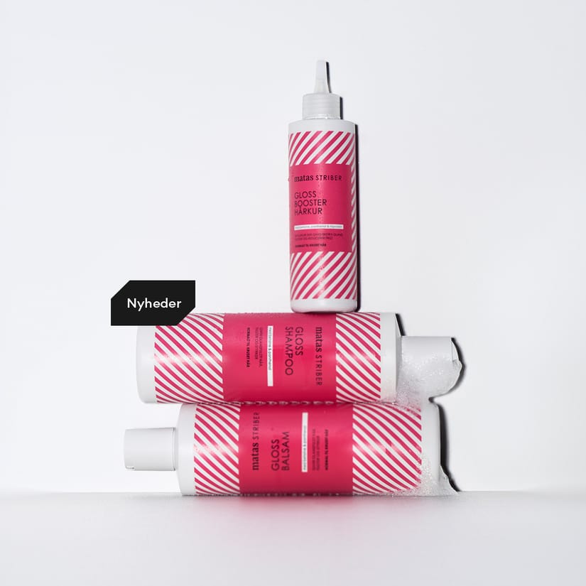 Tre pink Matas Striber hårplejeprodukter med Gloss Booster Hårkur, Gloss Shampoo og Gloss Balsam står stablet på hvid baggrund. En sort label med teksten “Nyheder” ses ved siden af.