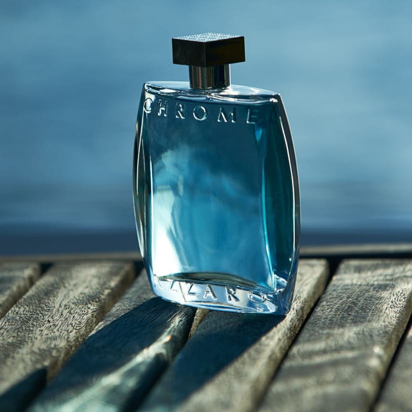 Her ses en Azzaro Chrome parfumeflaske på et træbord med en blå baggrund.